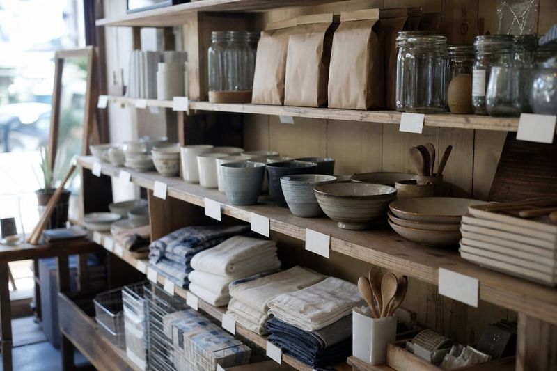 小さな雑貨店の棚。器や布巾、瓶が並び、白い値札が付いている